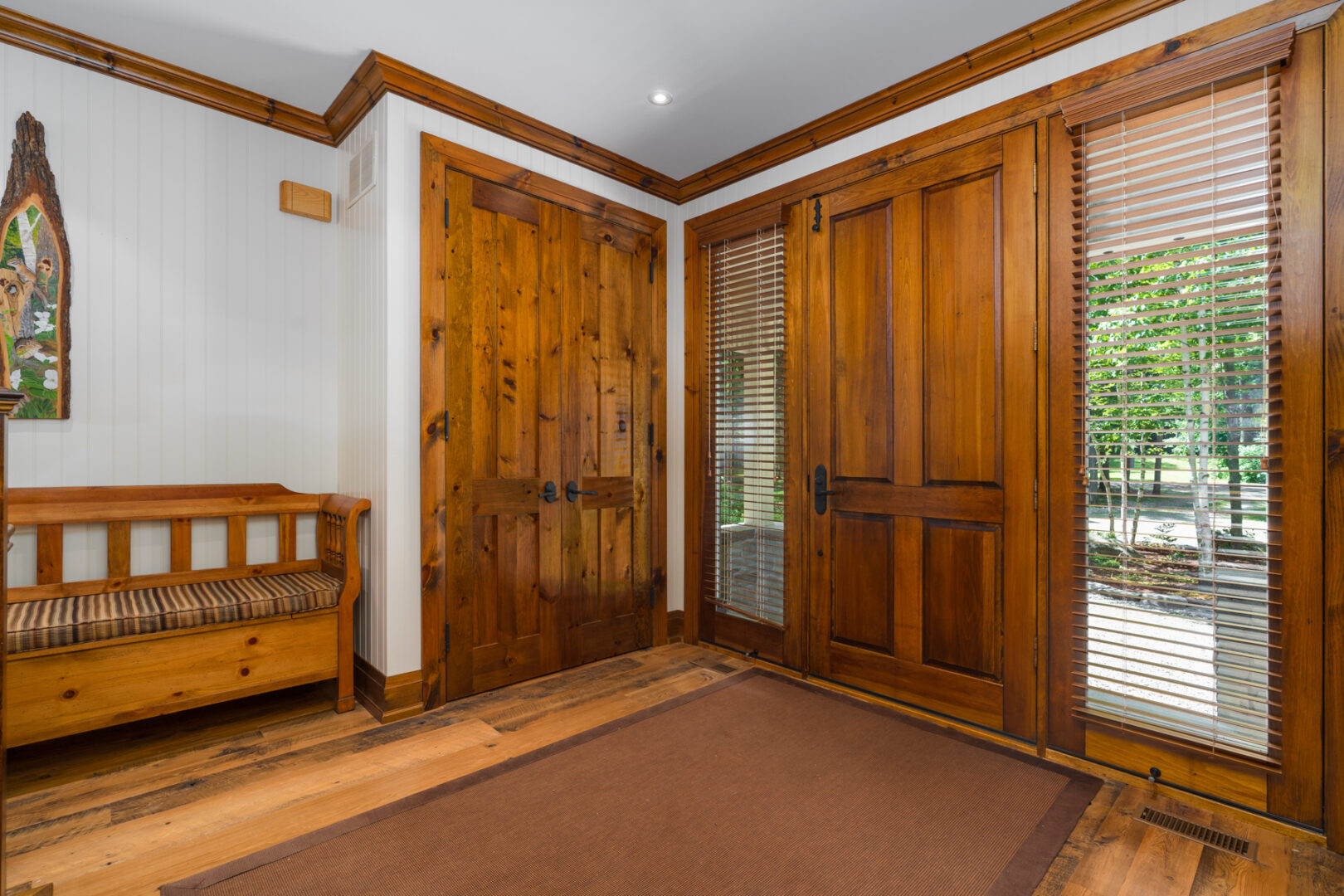 A large entryway of a house with a warm wood front door and hardwood floors.