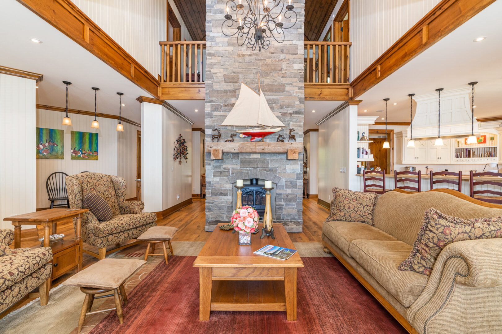 A bright, open-concept living area with a central stone fireplace and couches that opens into a kitchen off to the side.