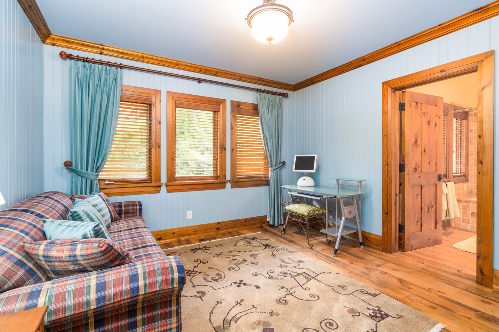 A small room with a couch and bright windows, with a doorway leading to a bathroom.