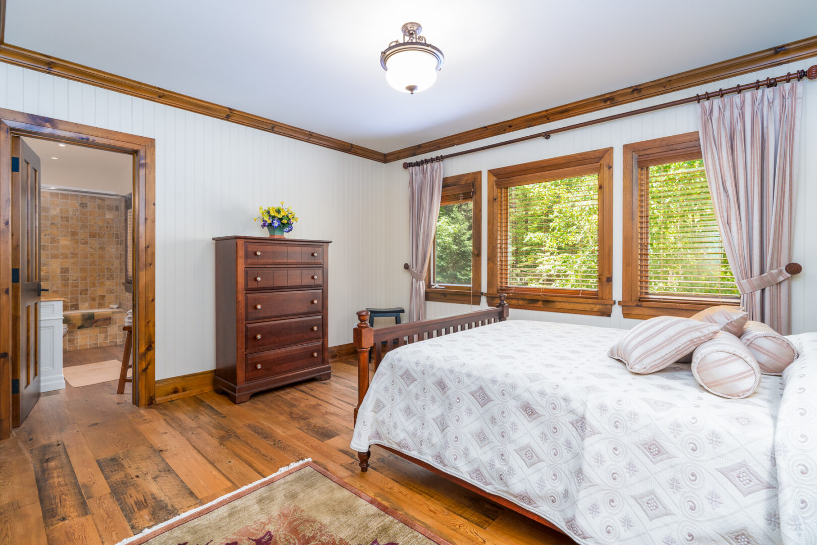 A bedroom with a small bed and large windows, with a doorway leading to a bathroom.