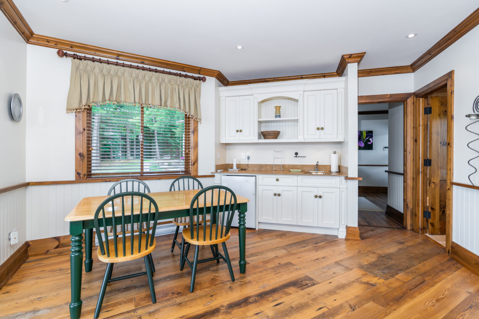 A spacious boathouse living space with large windows overlooking the lake, a small dining table, chairs, and a kitchenette space..