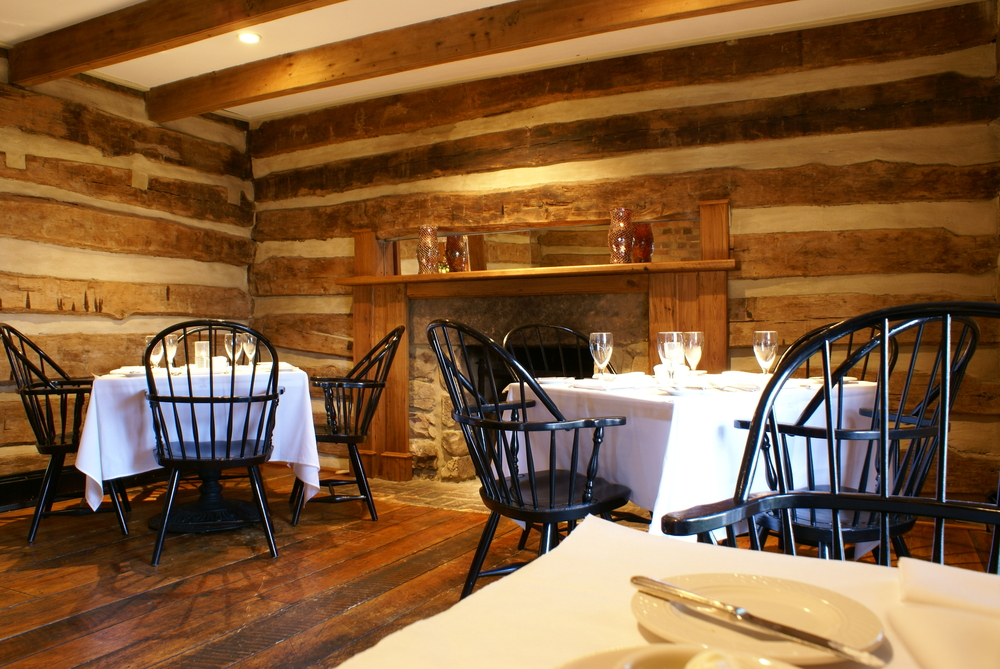 Vintage Windsor chairs around a rustic wooden cottage dining hall with white tables set for dinner