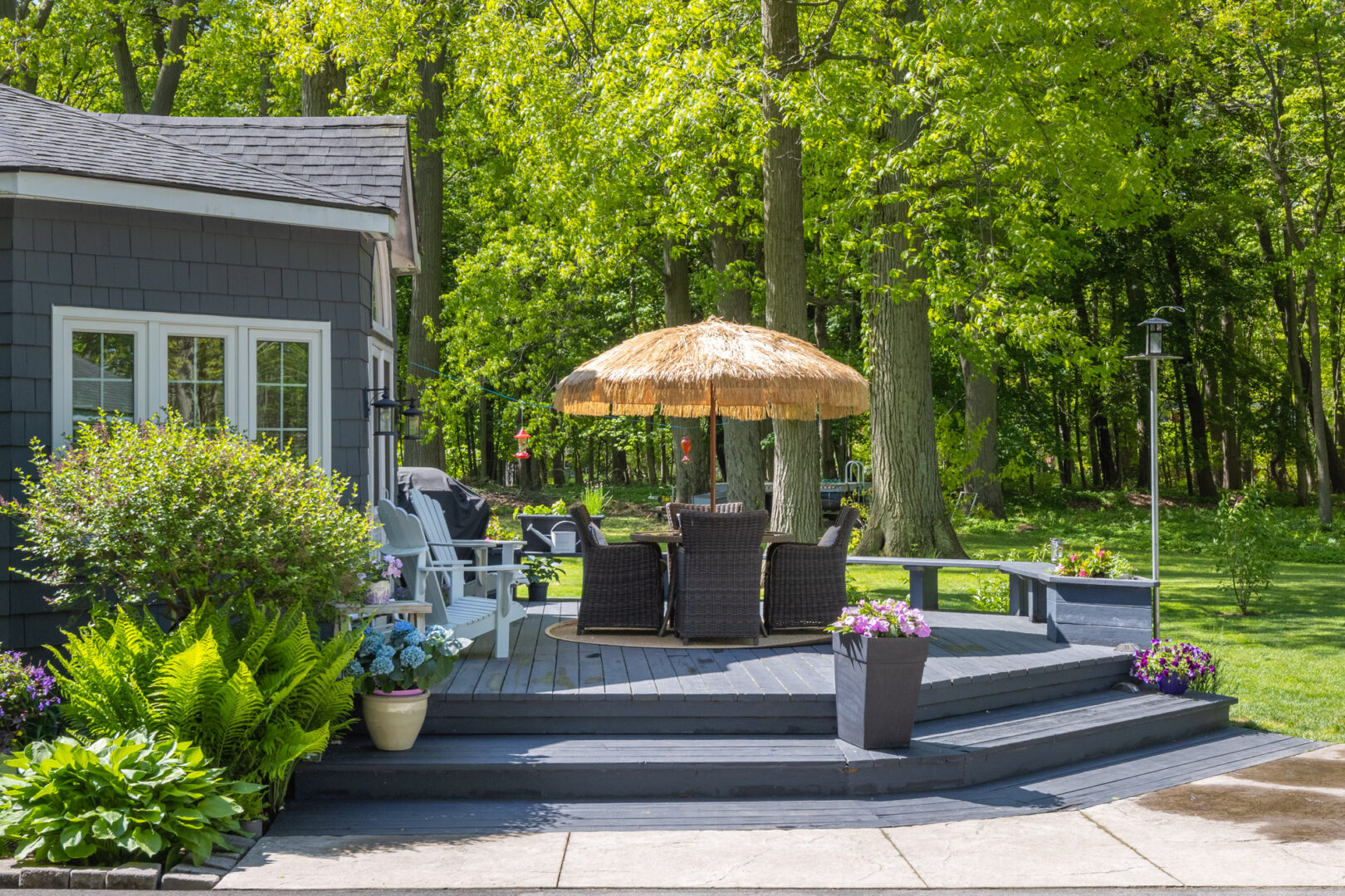 A small, round back deck area off a big cottage. Chairs surround a table with an umbrella in the center of the deck.