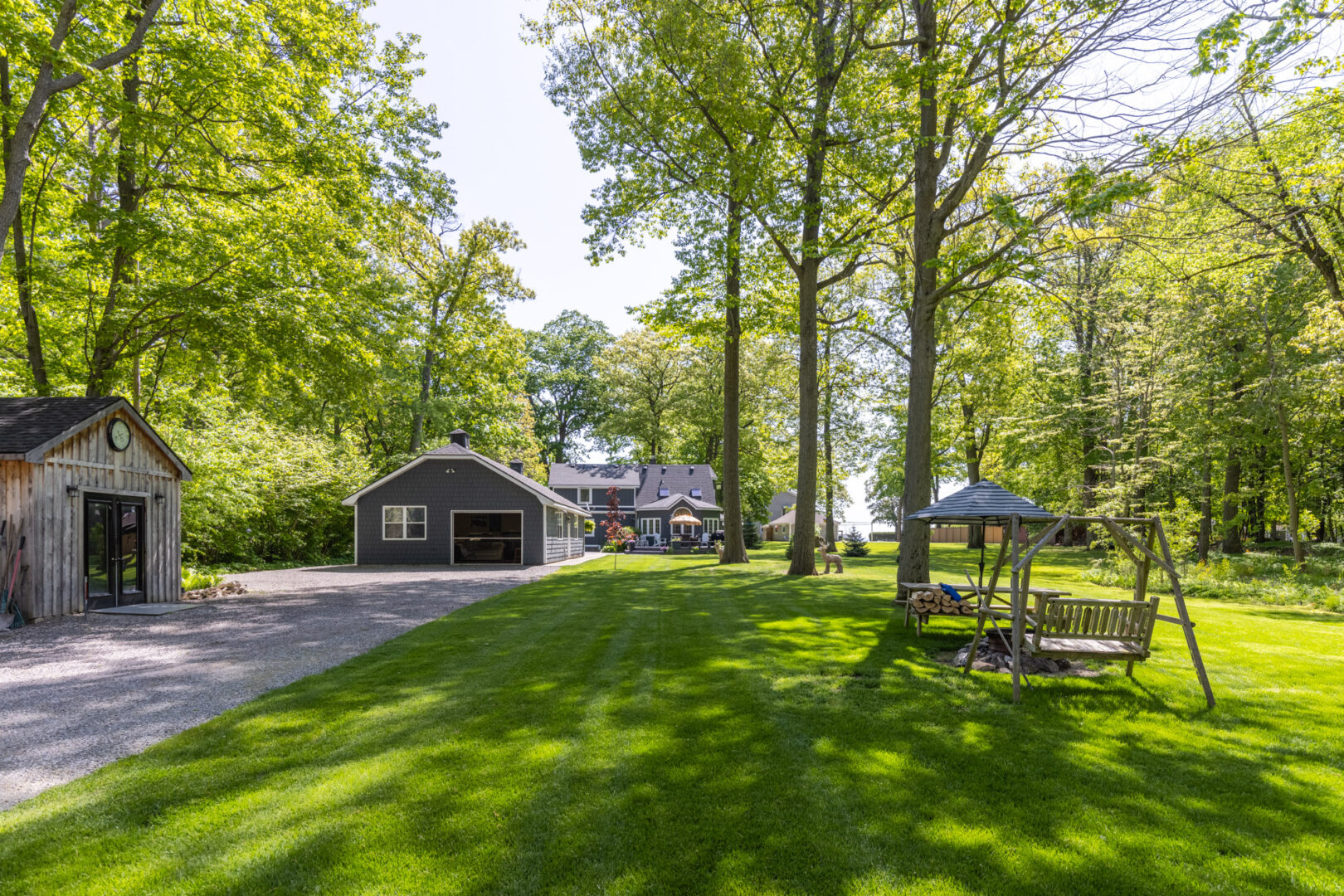 A spacious, manicured, grassy area surrounds a large cottage property. A long driveway leads to a shed, a detached garage, and a big cottage.
