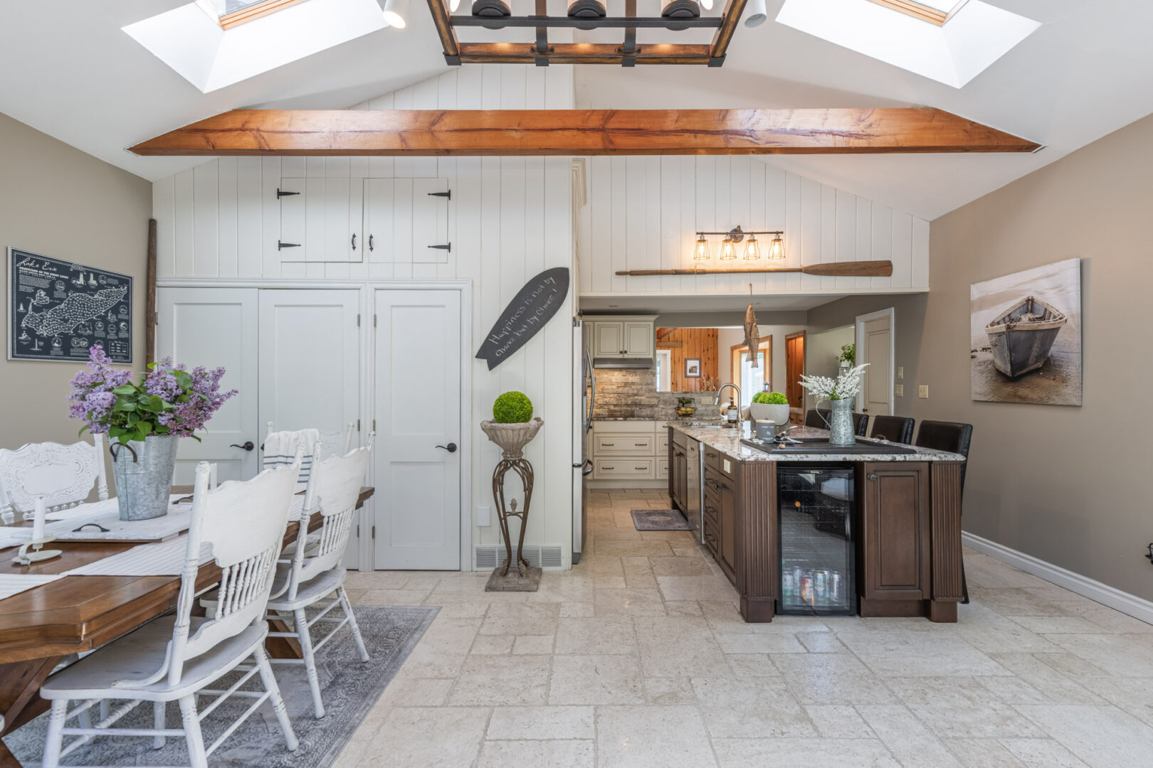 A bright, luxury cottage kitchen and dining area with white cupboards, light wood accents, and a dark granite kitchen island.