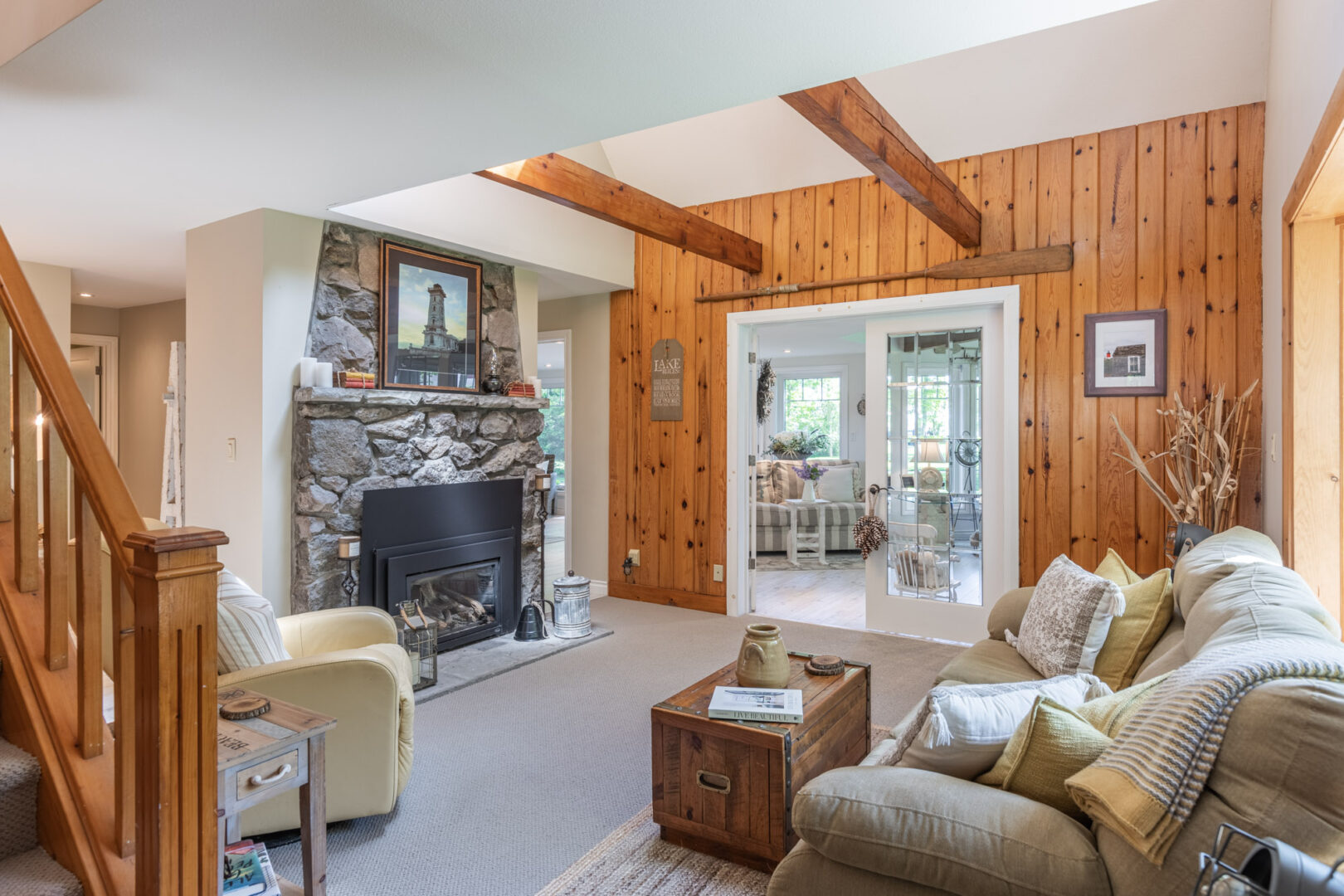A cozy but bright cottage living space with seating, a wood-panelled accent wall, and a gas fireplace.