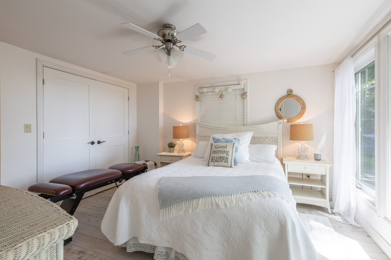 A bright bedroom with a large bed that has white bedding, two side tables, a closet, and a ceiling fan.