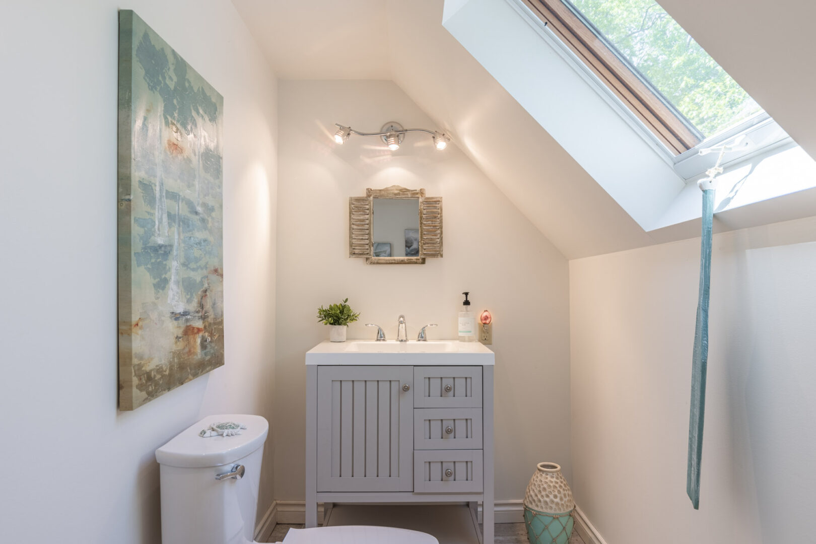 A small bathroom with a toilet, a sink, and a window in a slanted ceiling.