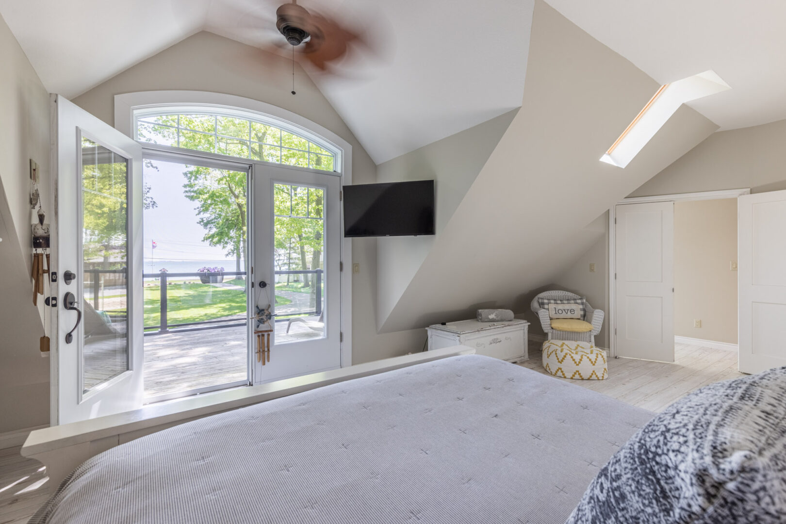 Double doors leading out to a balcony off a large, bright primary bedroom with a big bed.