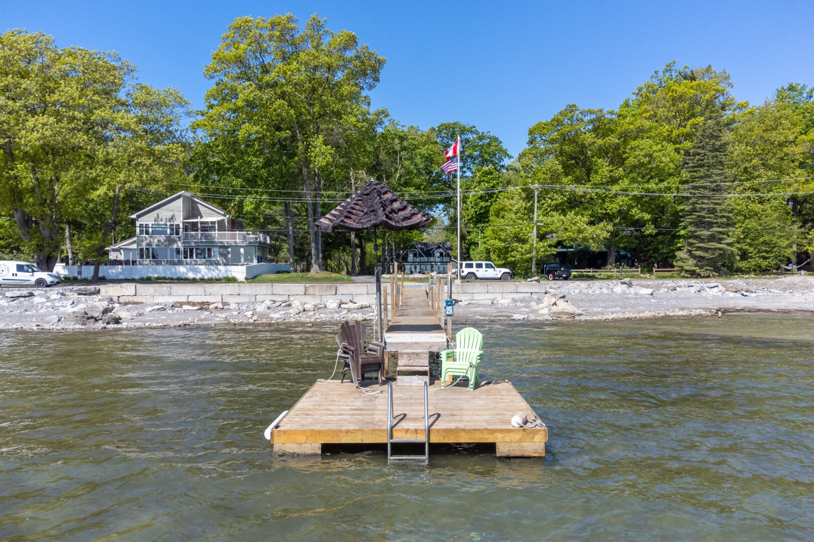 View of the end of a long dock from the lake. Two chairs and an umbrella sit on the end of the dock, overlooking the water.