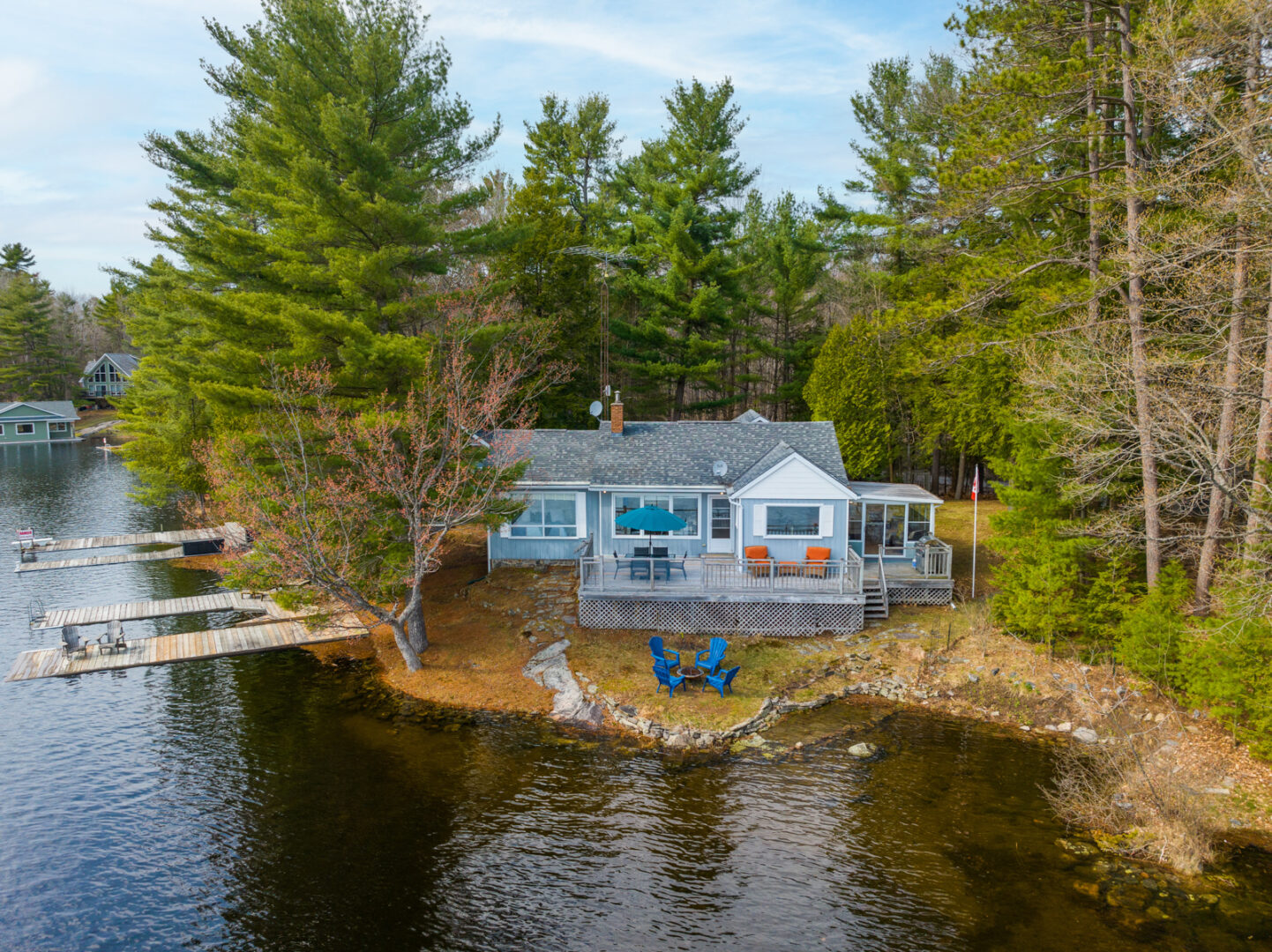 A cottage sits on the shoreline of a lake, surrounded by trees.