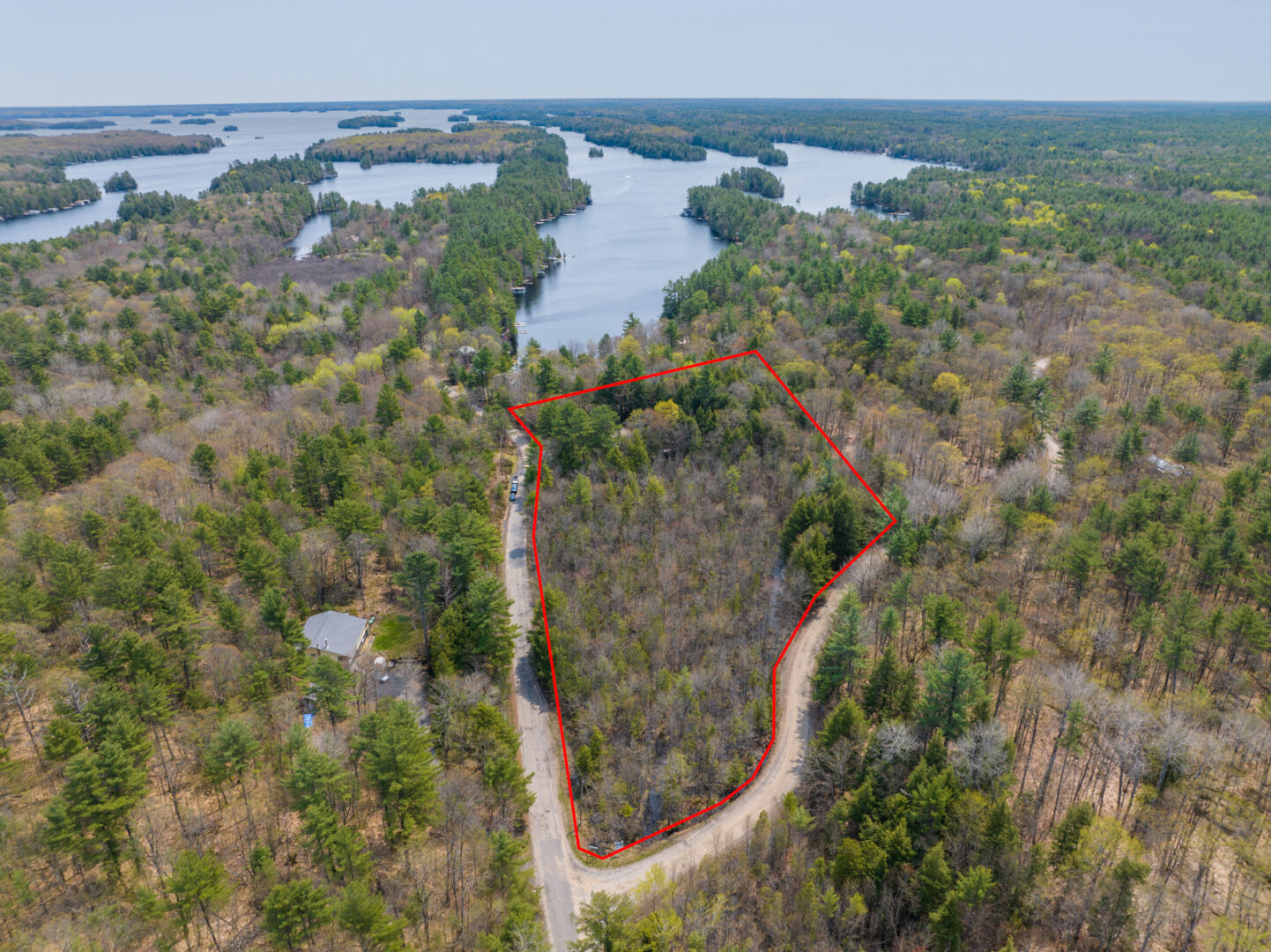 A fork of land is outlined in red, indicating the property area of a cottage. Trees and roads surround the area, and there is a lake in the background.
