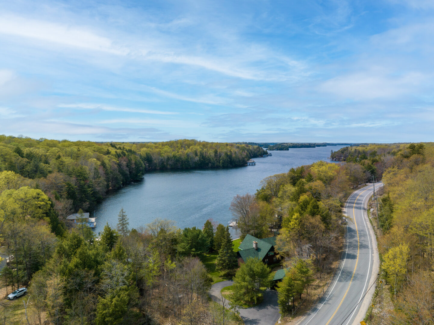 A large cottage sits in a stretch of land between the road and the lake. Thick trees line the narrow peninsula of lake on either side.