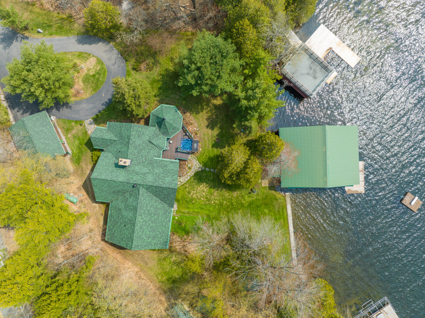 Aerial view of a large cottage with a green roof on the water, with a boathouse just off the shore.