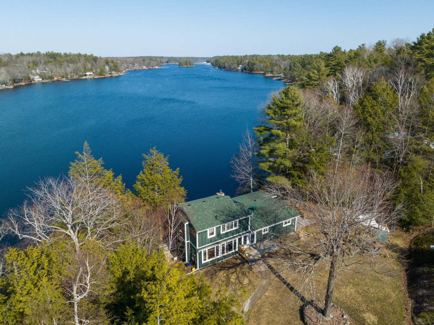 A big cottage sitting on the shoreline of a blue lake, surrounded by trees.
