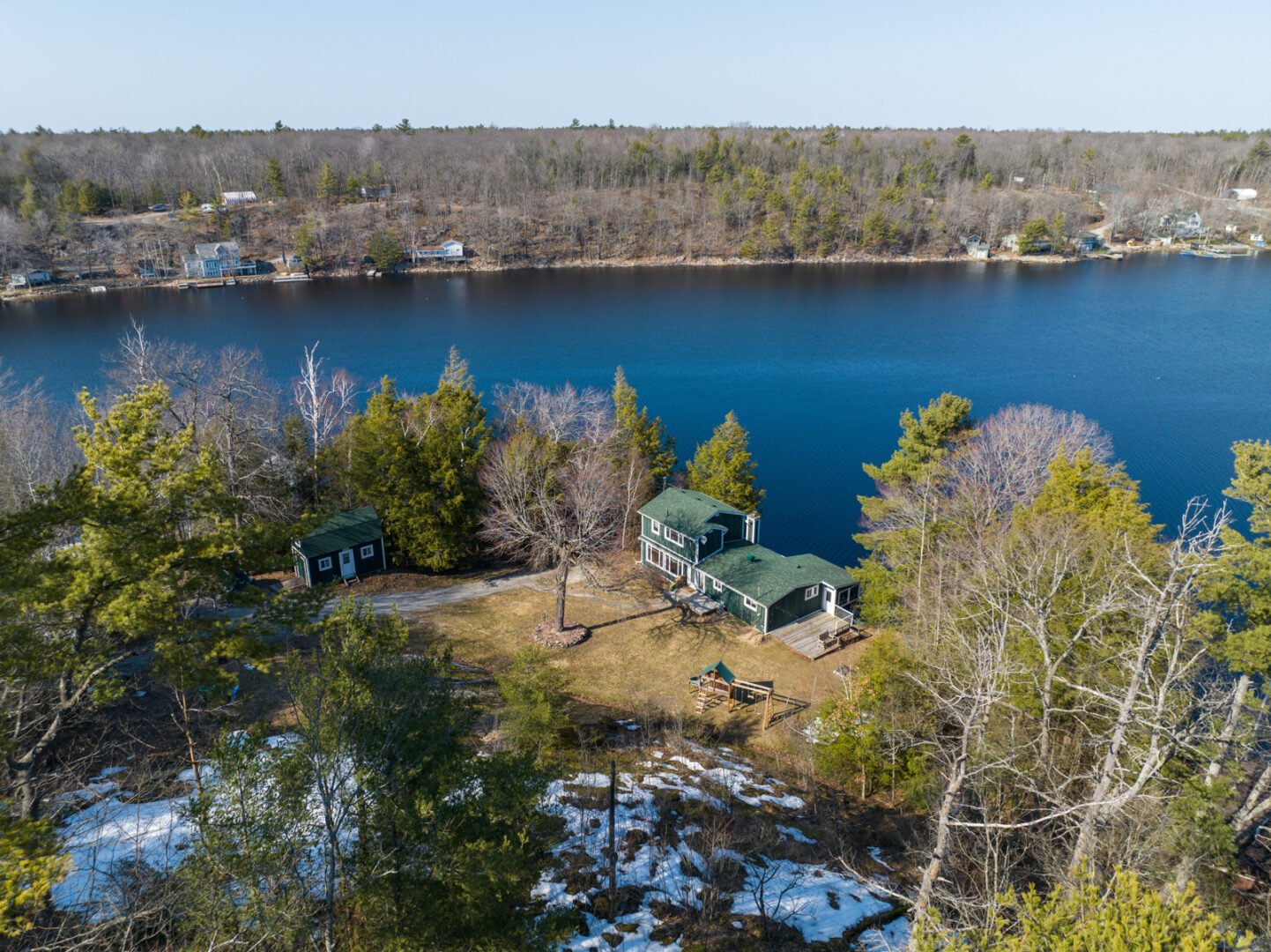 A cottage property with a main cottage and a small bunkie sit surrounded by trees, lakeside.