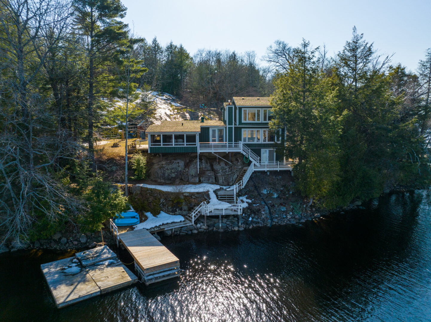 A large cottage with lots of windows sits on the shoreline of a lake. A large dock extends into the water.
