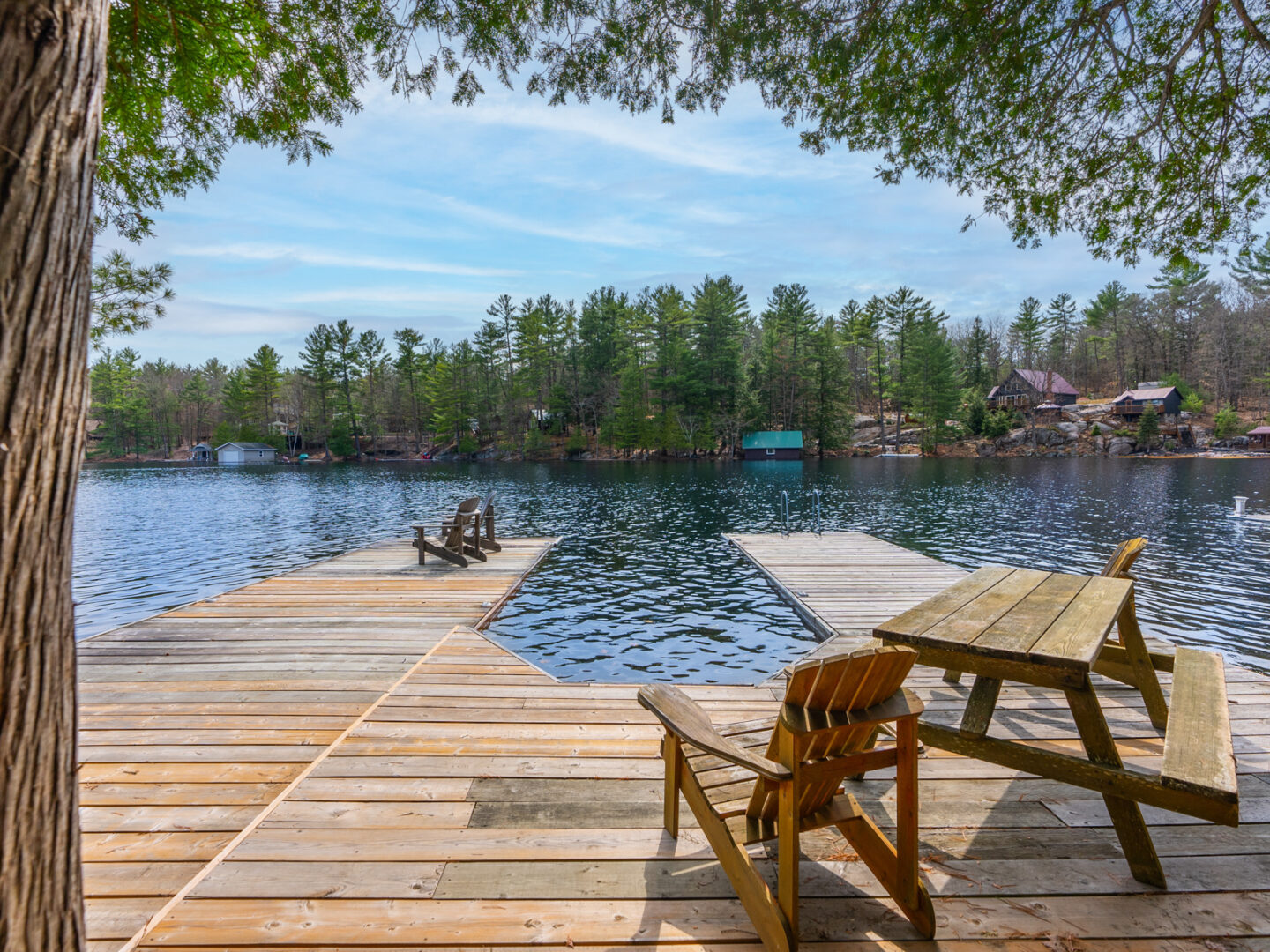 A long, U-shaped wooden dock extends into a calm lake. Green trees can be seen on the shore across the water.