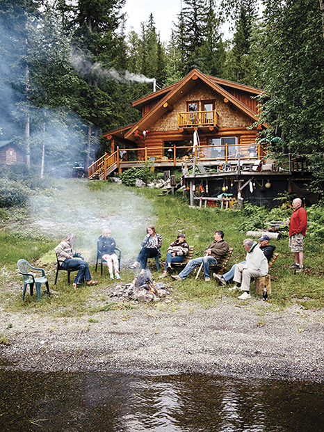 The family sits around the fire in front of the lodge