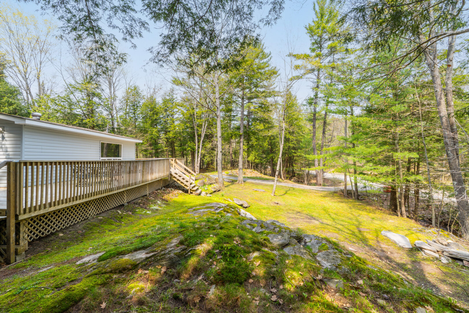 A large, sloping outdoor space at the side of a small cottage, with grass and some rocky areas.