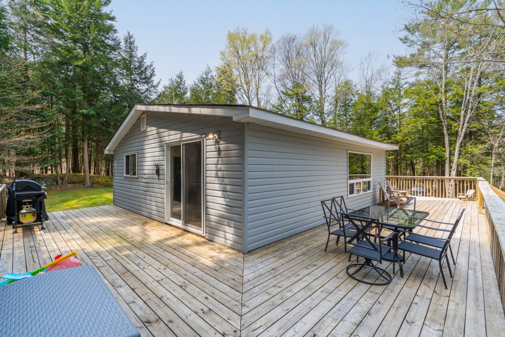 A large deck wraps around the corner of a small cottage. A dining table and chairs sit on the deck.