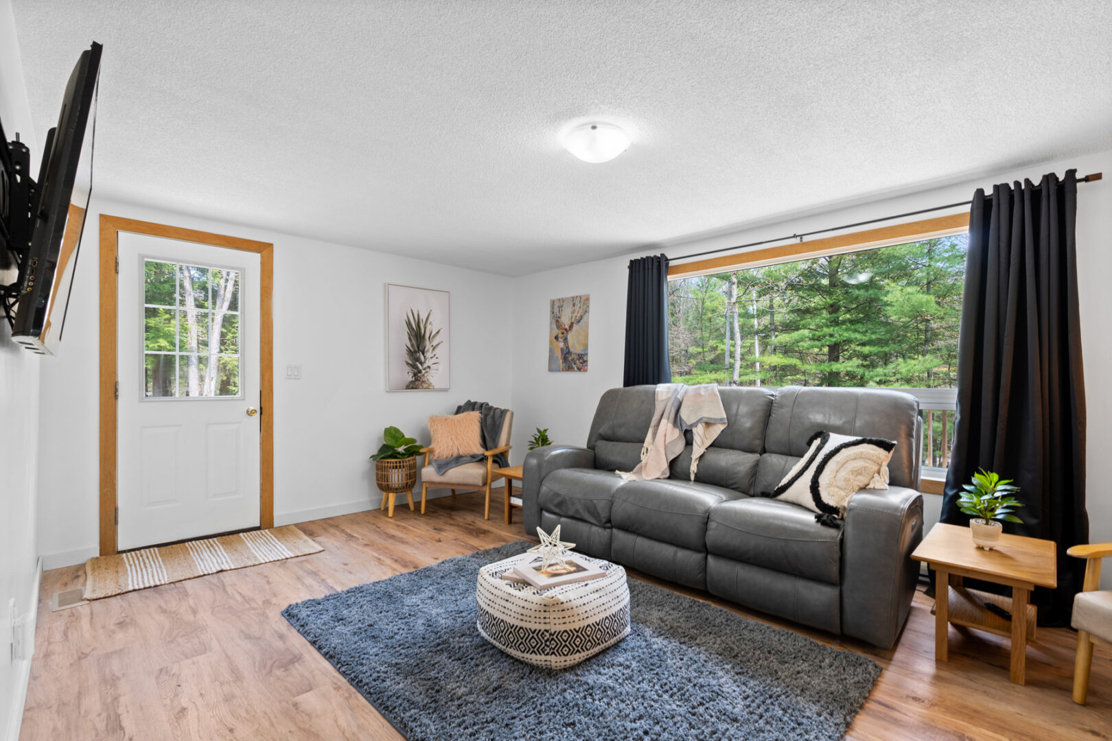 Inside of the front door of a small cottage, leading straight into a bright living area with a rug, a couch, and a large window.