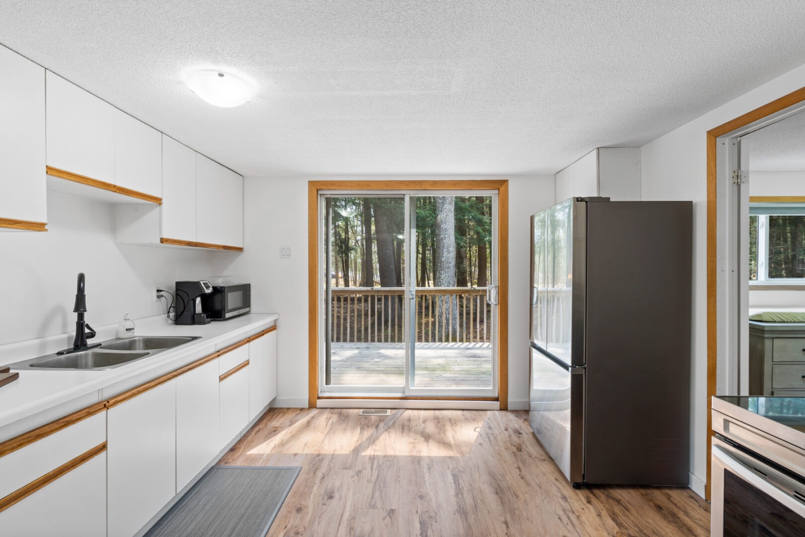 A small kitchen with white cupboards, a fridge, and double doors that lead to an outdoor deck.
