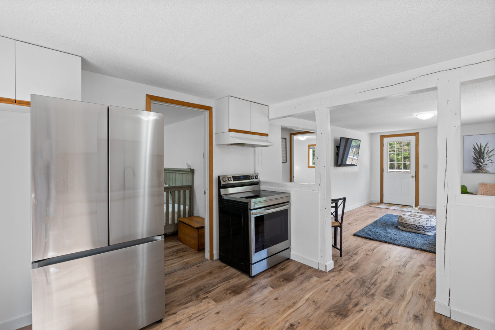 A small kitchen space with a stainless steel fridge and oven. A doorway off to the side leads to a small bedroom.