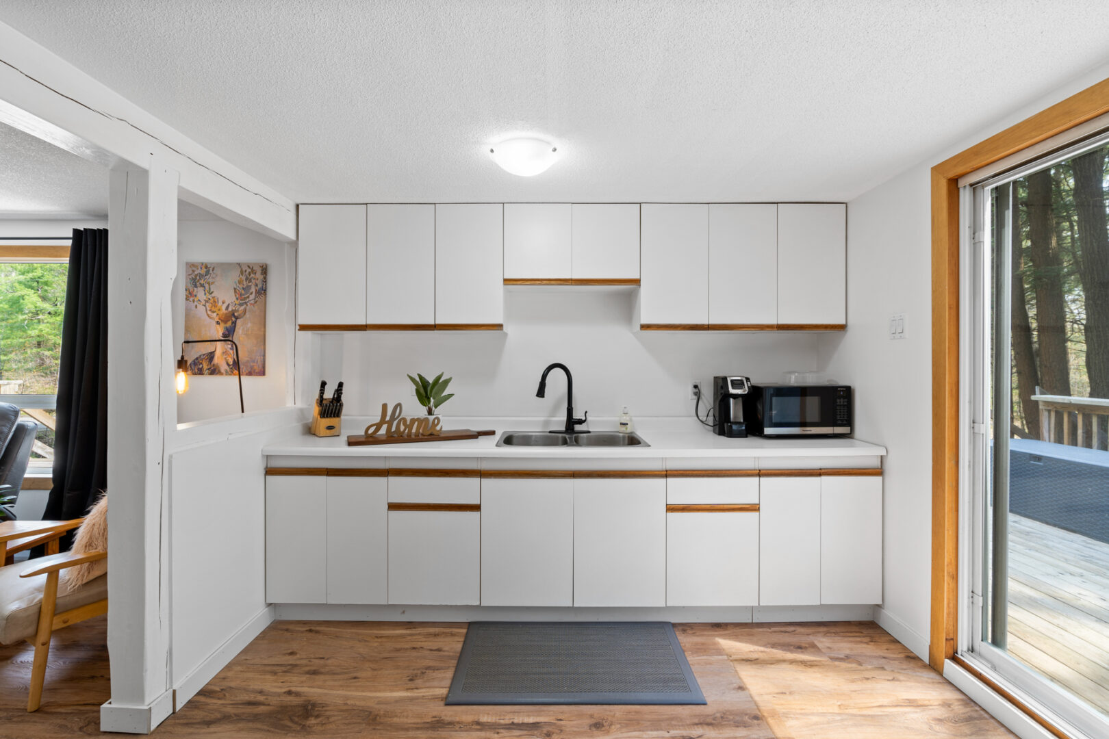 A small kitchen counter space with white cupboards, a sink, and a microwave.