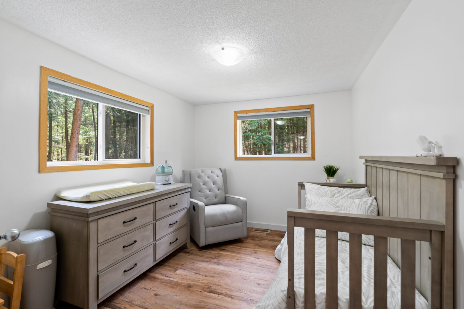 A small bedroom with a single bed, a chair, a short dresser, and two windows.