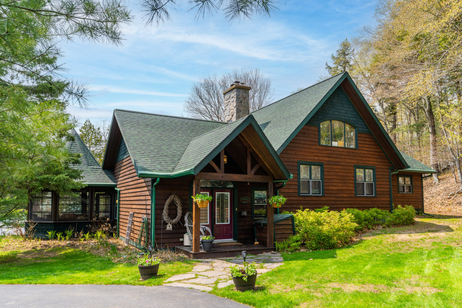 Front exterior of a large cottage with a landscaped front yard, a green roof, lots of windows, and a red front door.