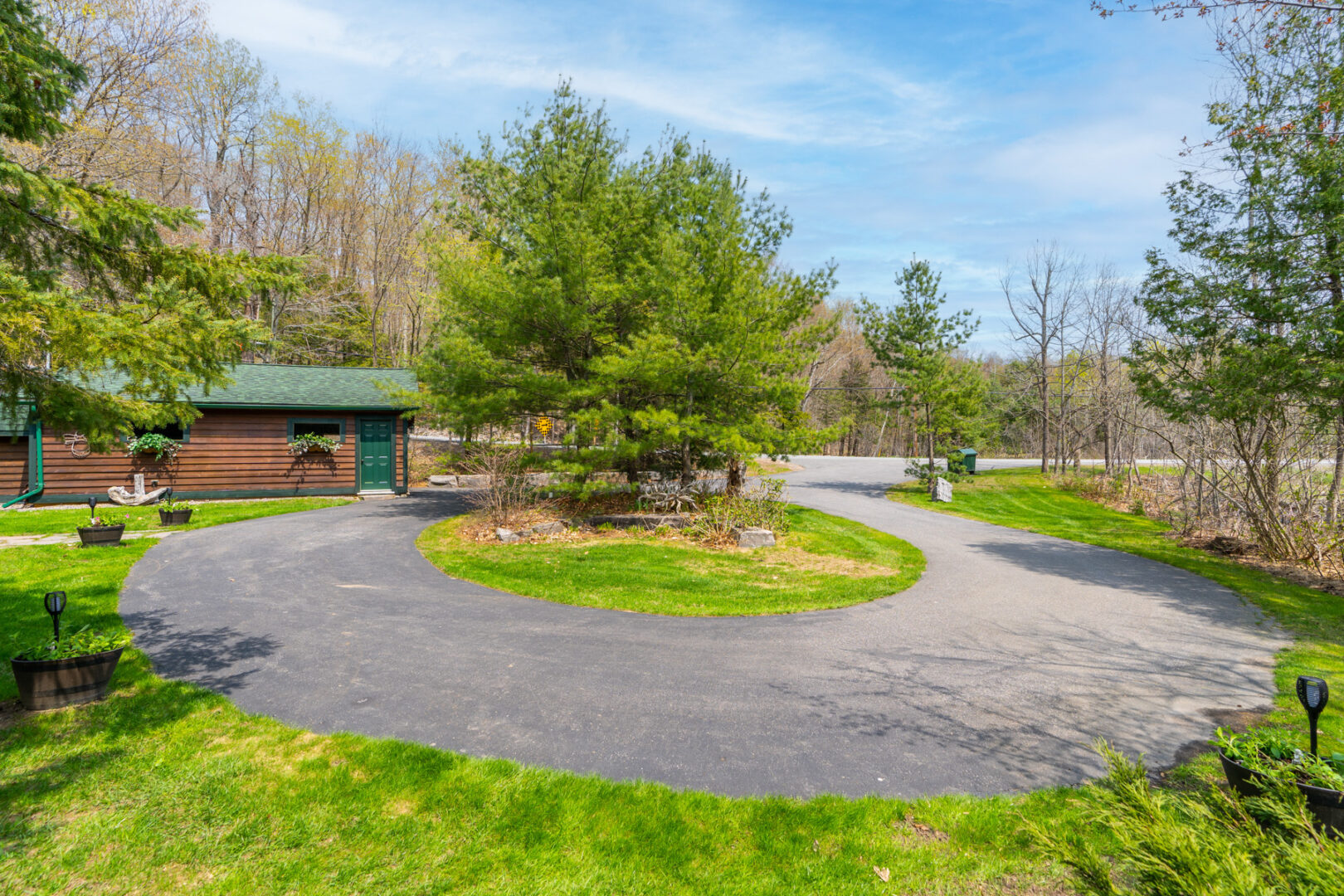 A large, circular driveway with a tree in the middle, surrounded by grass.