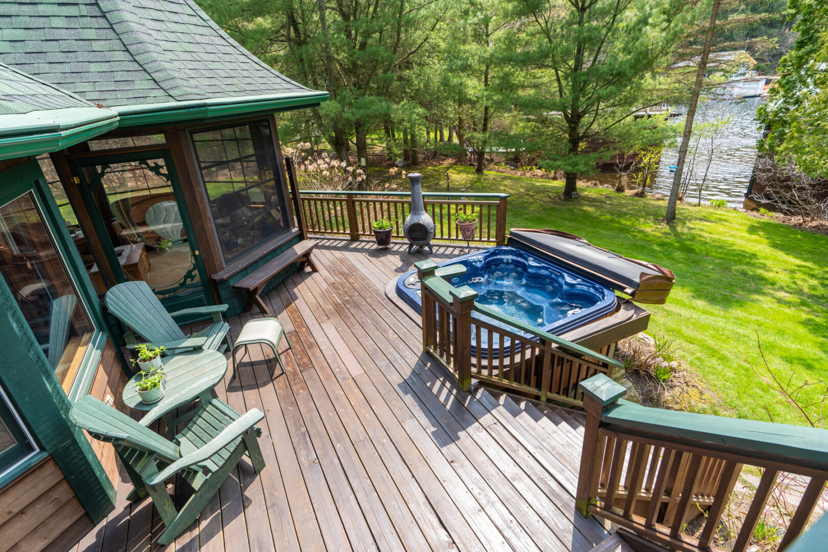 Looking down on a large deck area with chairs, a hot tub, and a screened-in room.