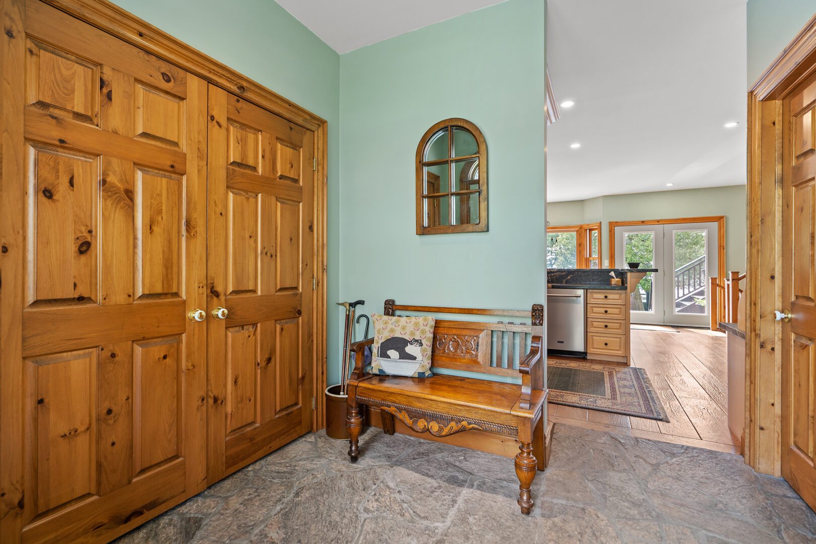 The entryway of a large cottage, with sage green walls and a big closet with wooden doors.