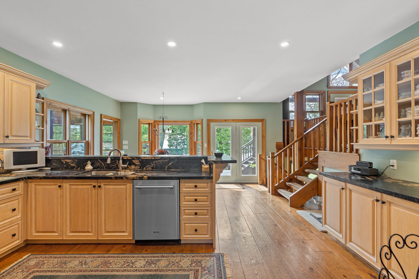 A bright, open space with a kitchen, open stairs to a living area, hardwood floors and big windows.