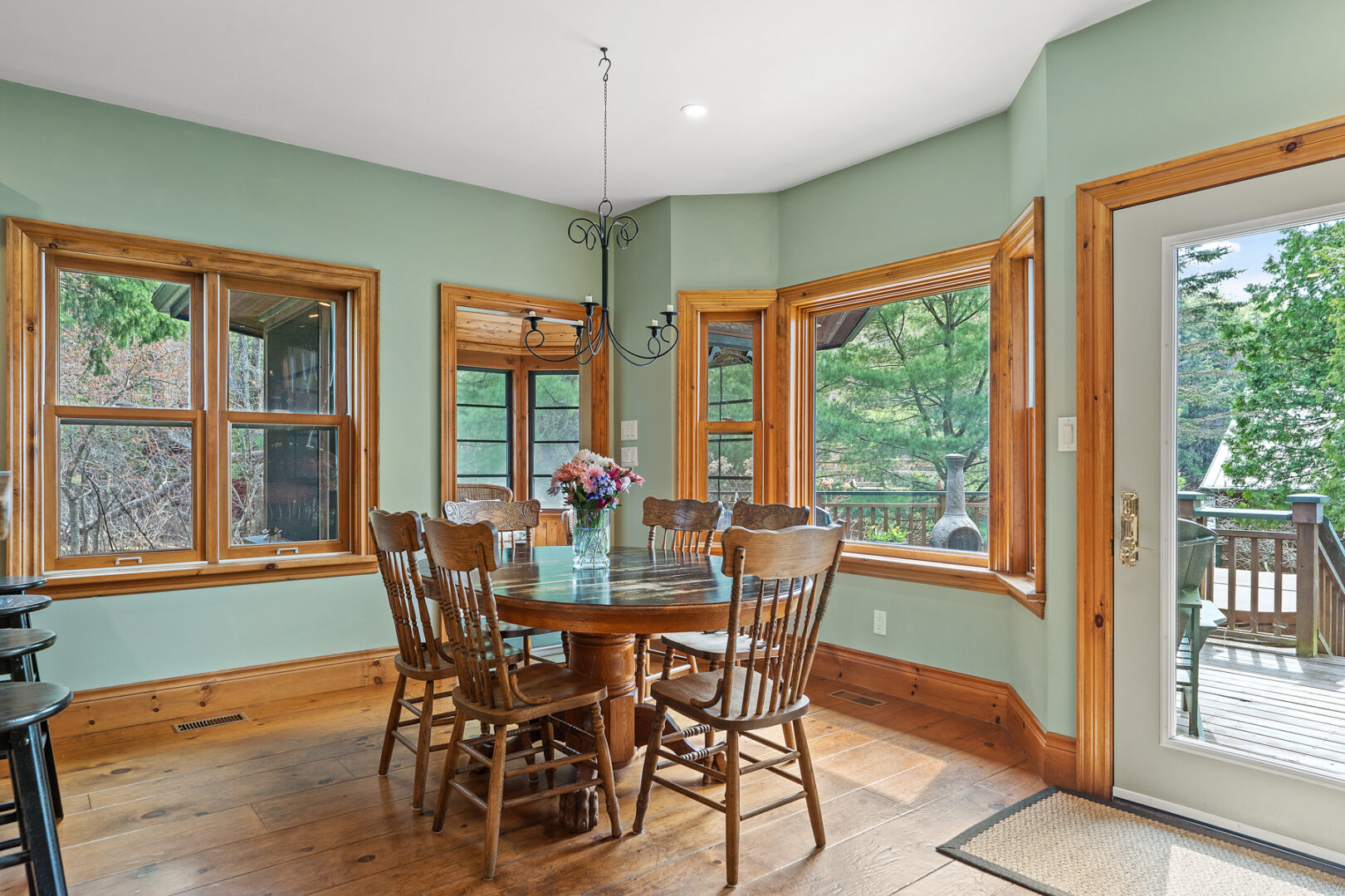 A bright dining area with a table and chairs, lots of windows, sage green walls, and hardwood floors.