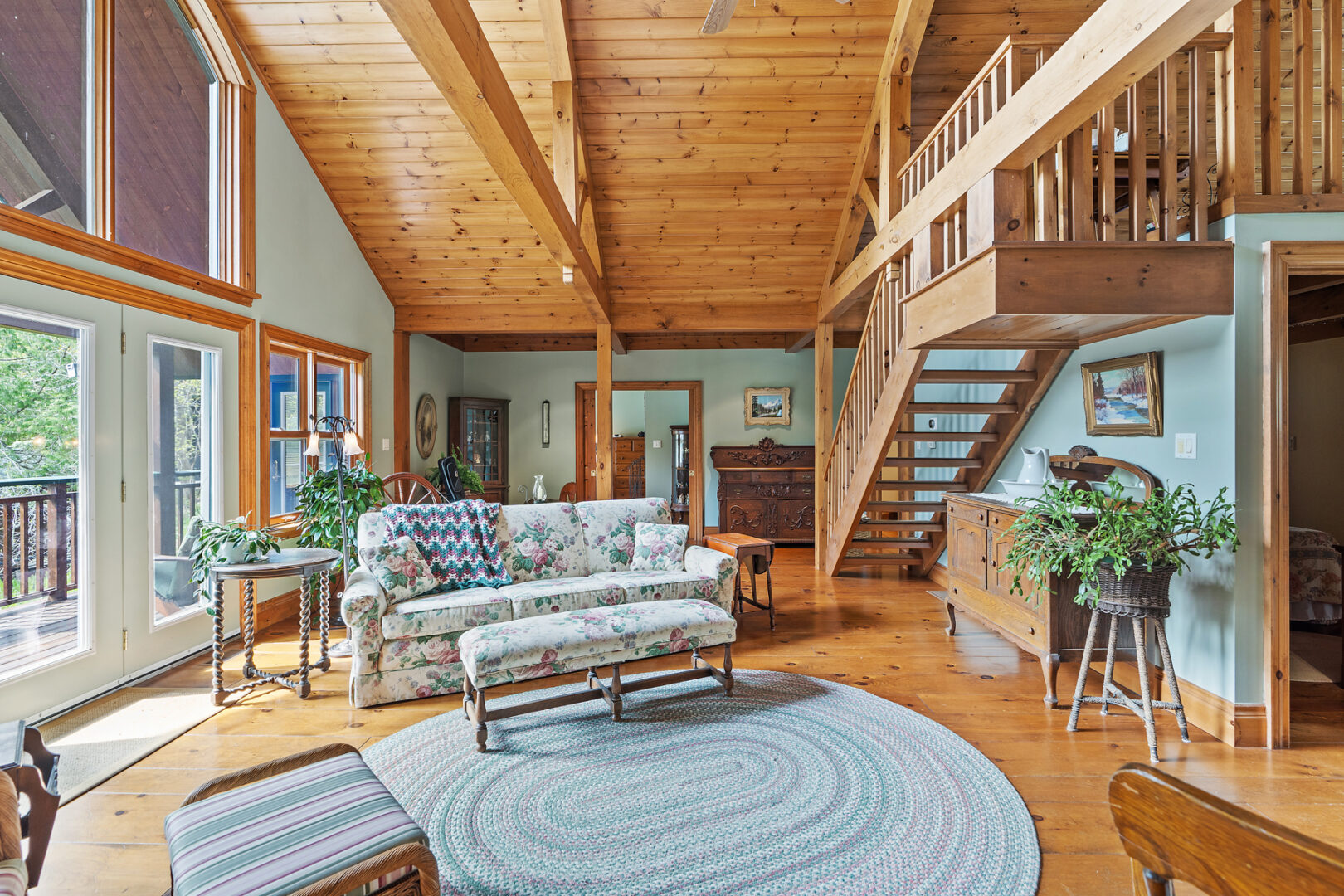 A bright, spacious living area with a couch, wood flooring and ceiling, and stairs leading up to a loft area.