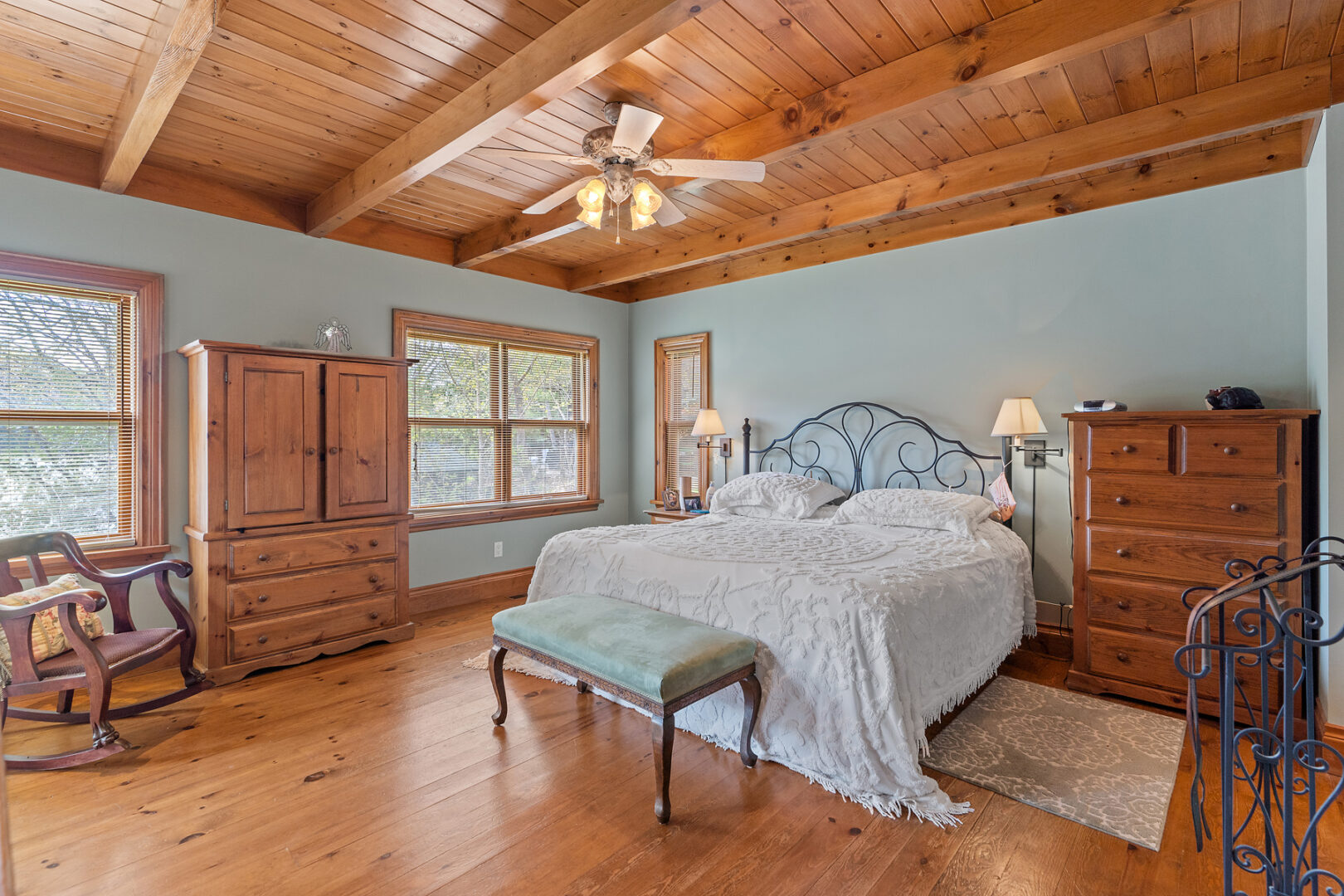 A spacious bedroom with a big bed, a wood-panelled ceiling, a wardrobe, and a window.