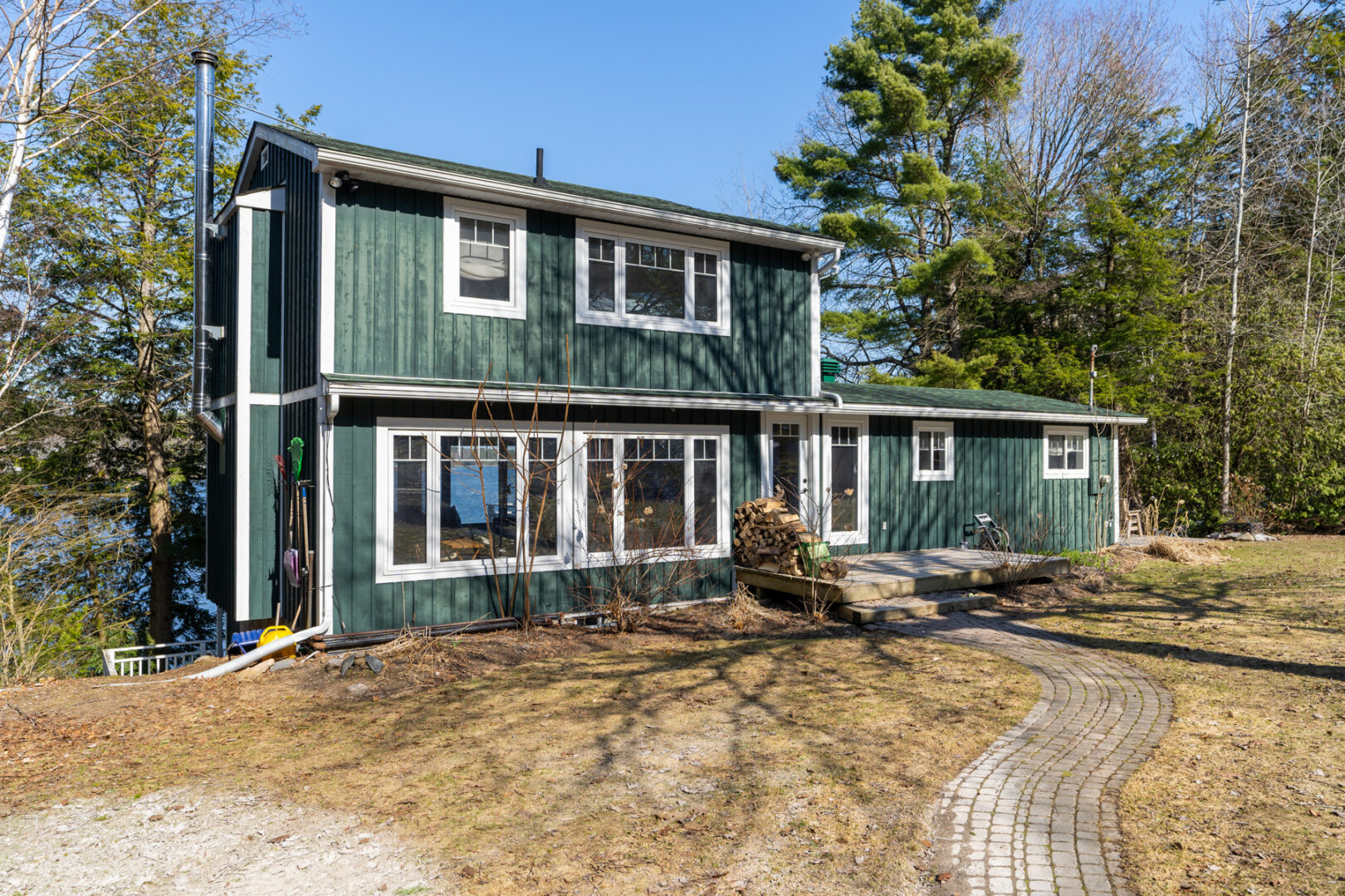 A green cottage with lots of windows sits in a grassy area.