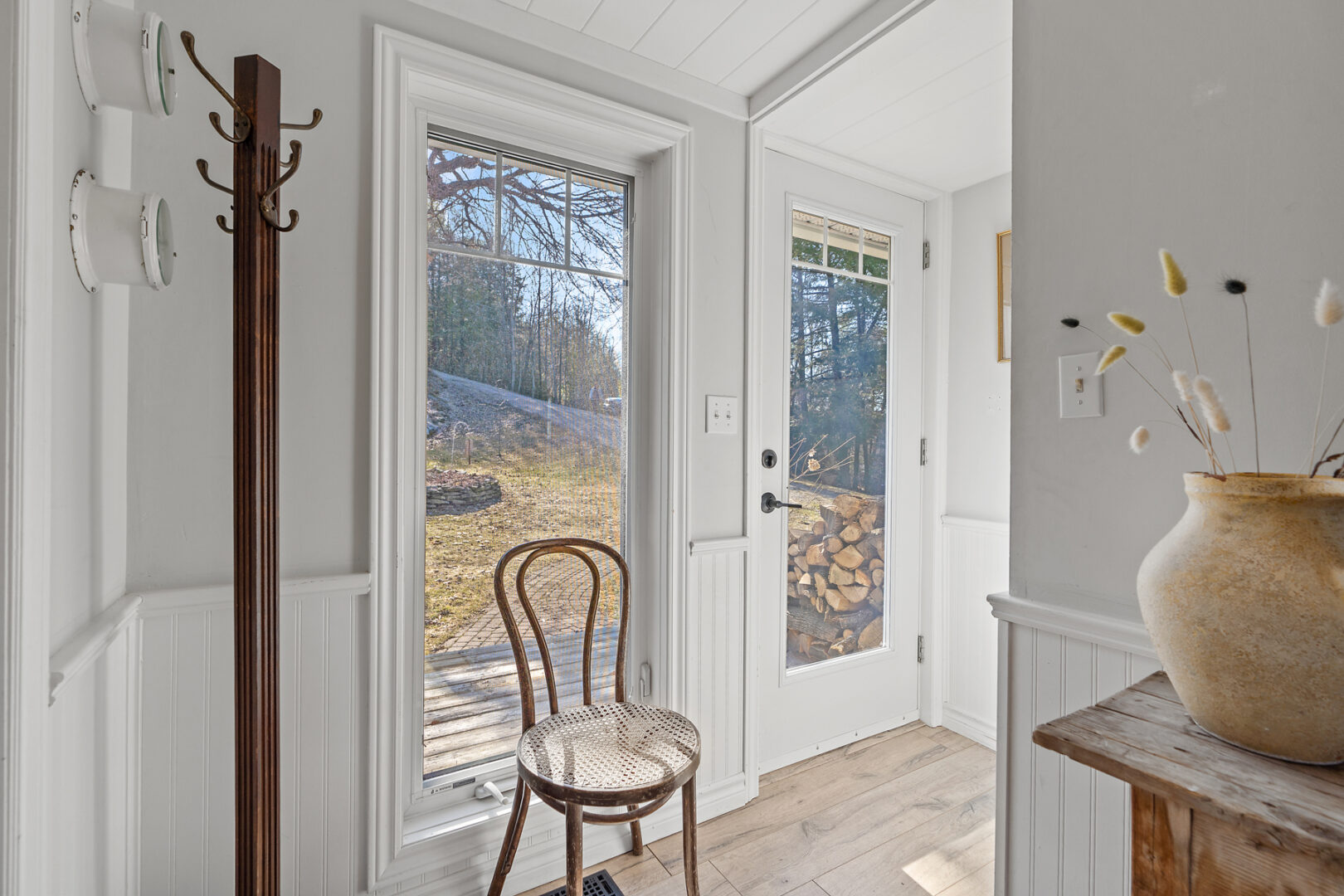A small, bright entryway of a cottage, with a front door and a chair inside the entrance.
