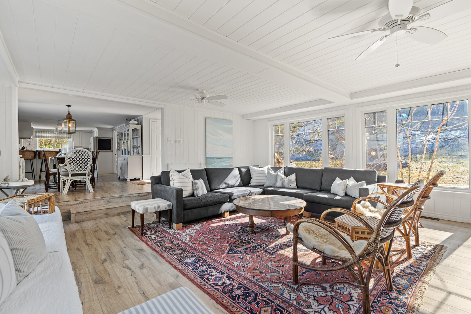 A large cottage, bright living area with a couch, an ornate rug, a coffee table, and large windows.