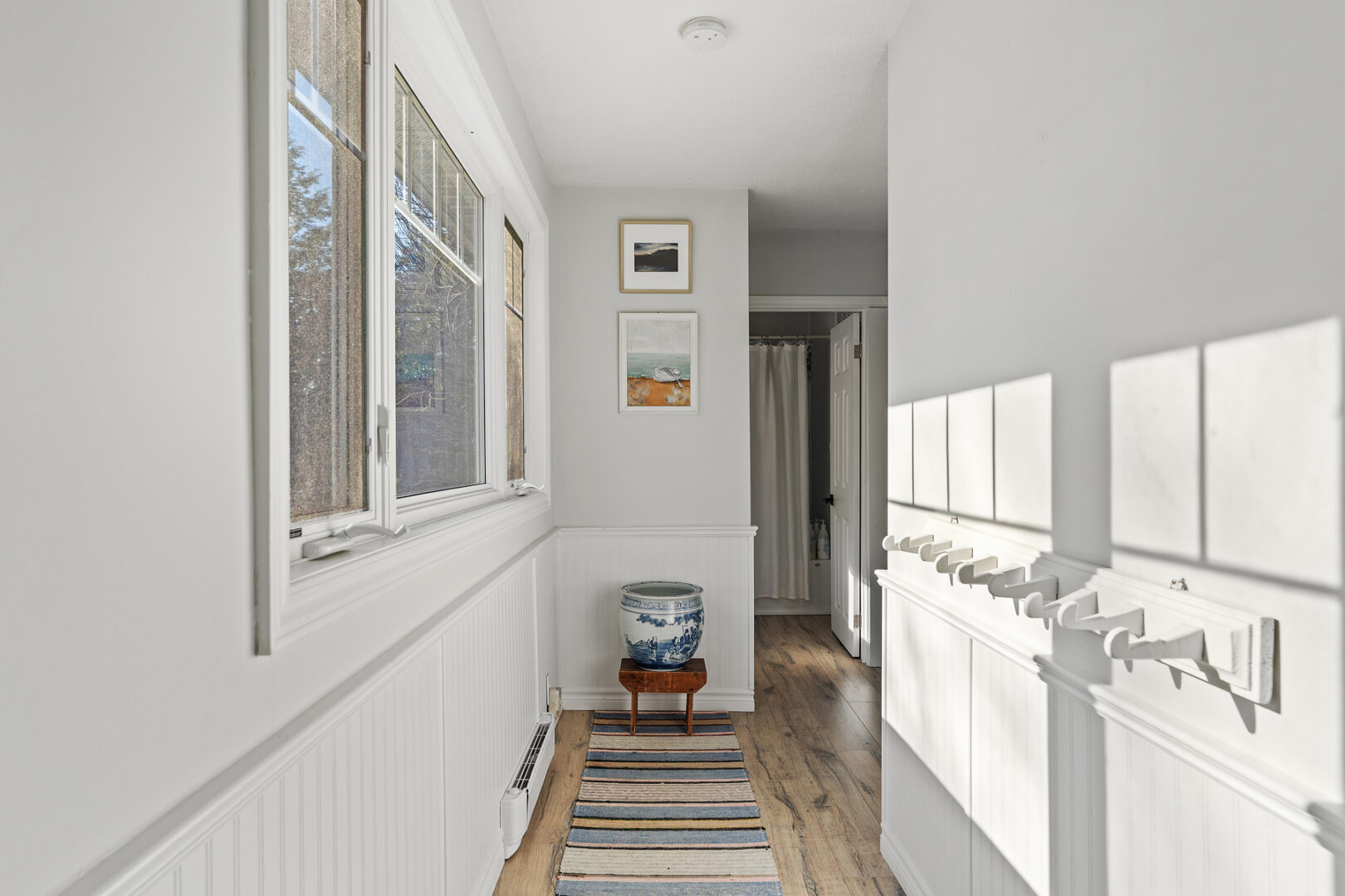 A narrow upper-level hallway with white walls and a big window.