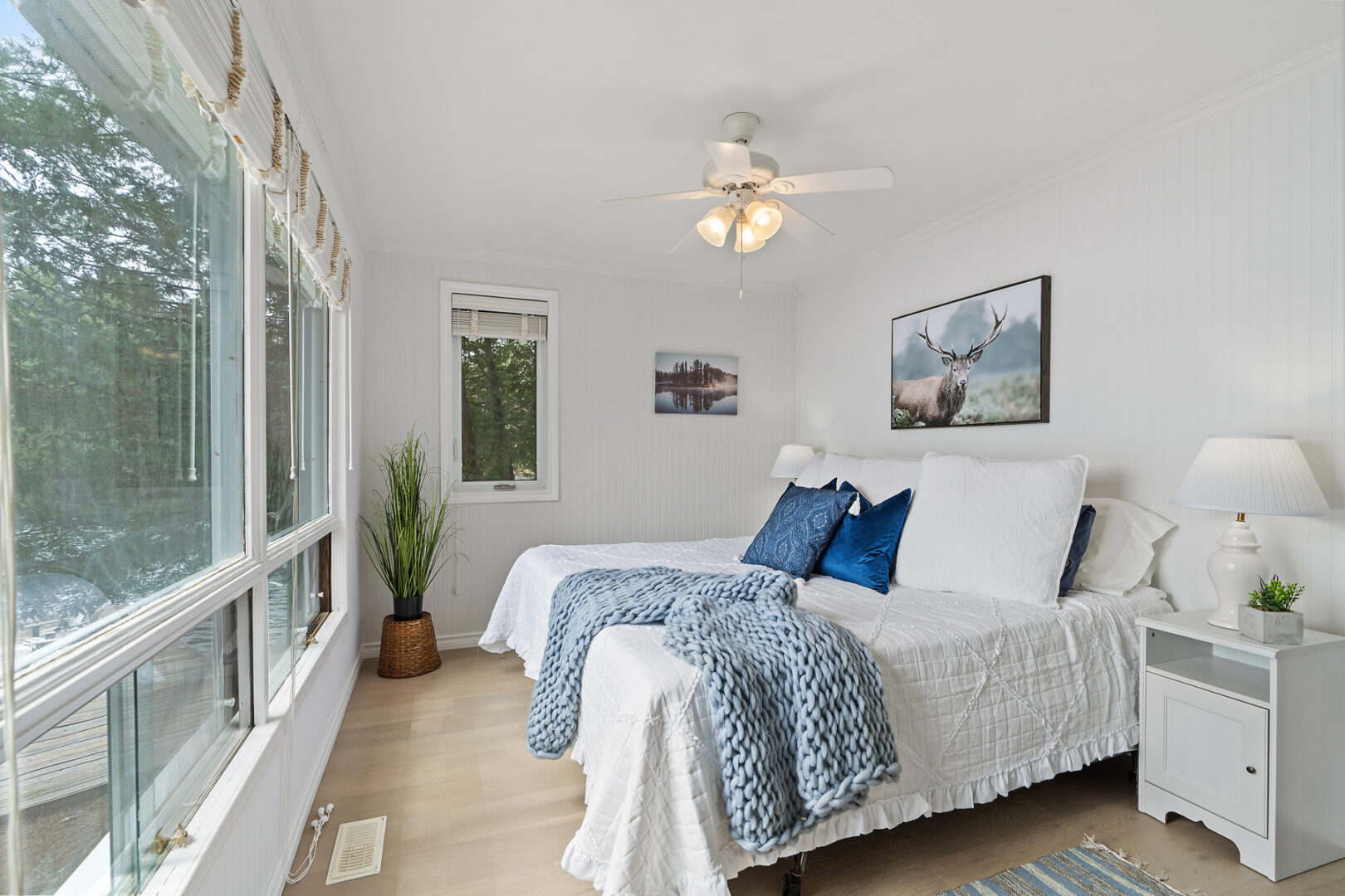 A bright bedroom with large windows and white and blue accents.