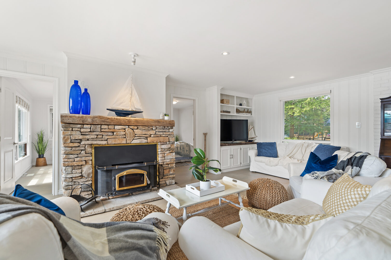A bright cottage living space with couches, a fireplace, and a television.