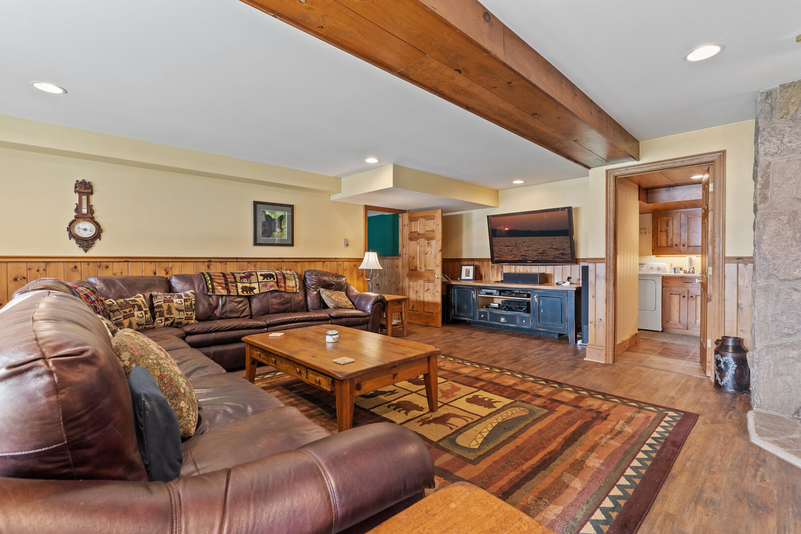 A large lower-level living space with a big L-shaped couch, a large area rug, and a television.