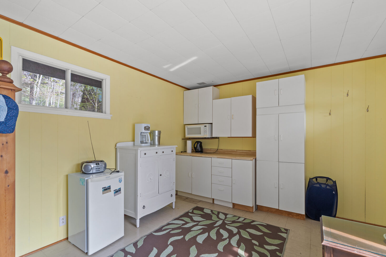 A small bunkie kitchenette with a mini fridge, a microwave, white cupboards, and yellow walls.