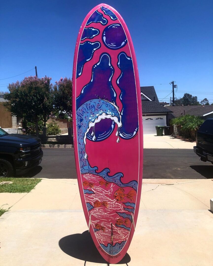 pink paddleboard with sun rays, a wave, and fishies