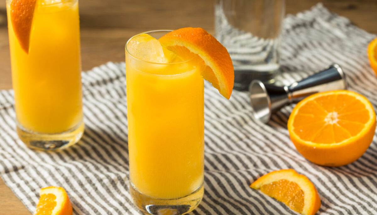 Two screwdriver cocktails with orange slices sitting on striped cloth