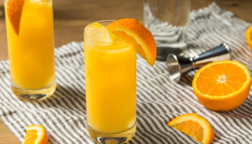 Two screwdriver cocktails with orange slices sitting on striped cloth