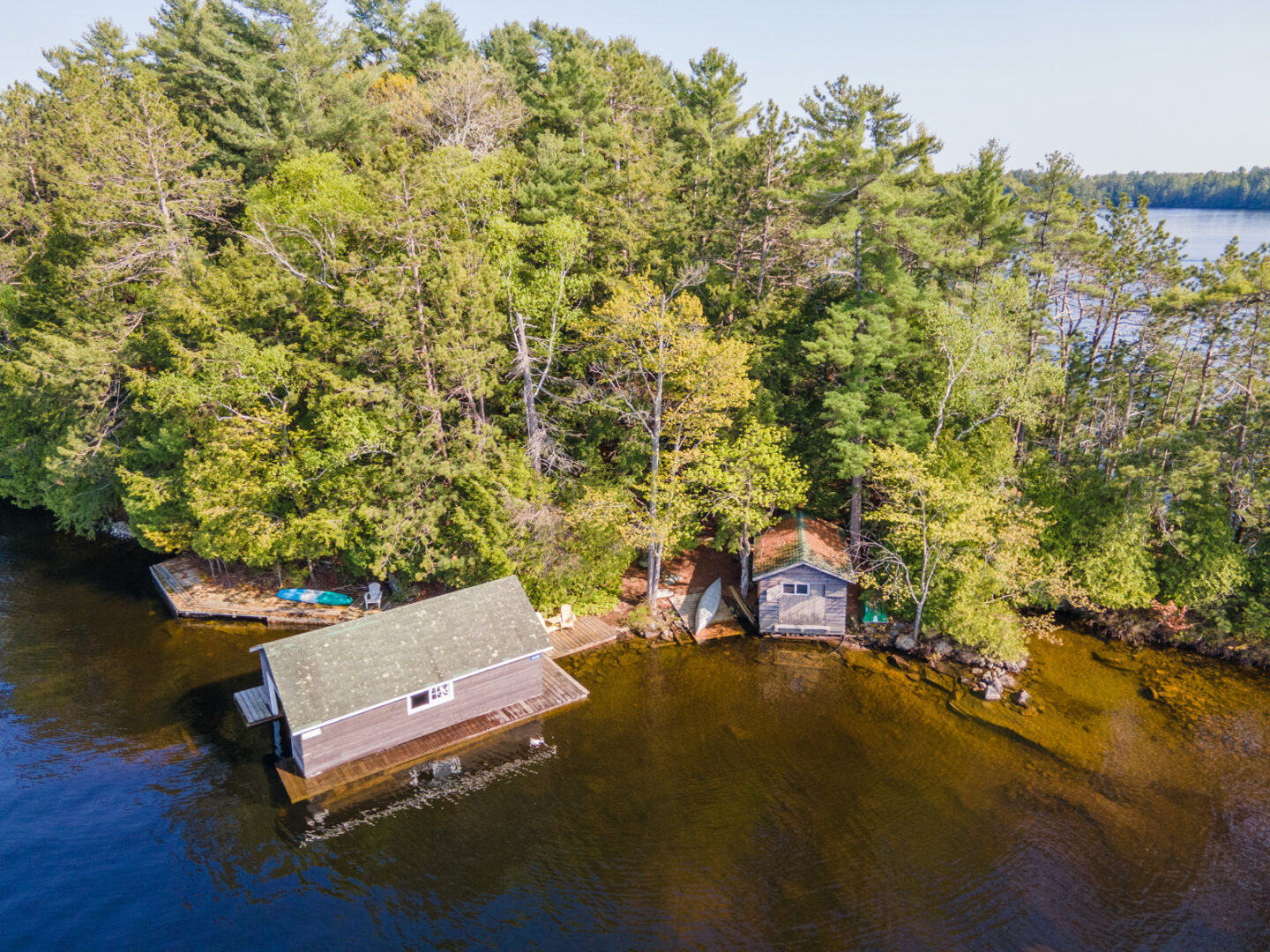 A boathouse and a small bunkie sit on the shoreline of an island peninsula on a blue lake.